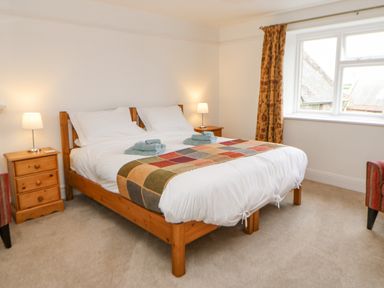 A bedroom with a wooden double bed two bedside tables with lamps a window with curtains and a patterned runner on the bed at Crookham Dairy in Crookham near Etal