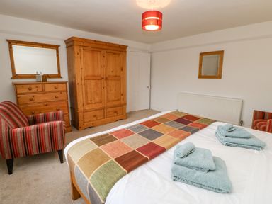 A bedroom with a double bed, wooden wardrobe, chest of drawers, two striped armchairs, and folded towels on the bed at Crookham Dairy Crookham near Etal