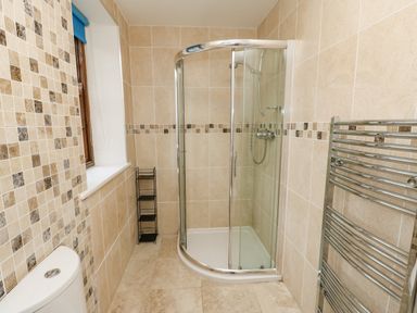 A bathroom with a glass shower enclosure a toilet a heated towel rail and tiled walls at Crookham Dairy in Crookham near Etal