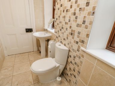 A bathroom with a toilet a pedestal sink tiled walls and floor at Crookham Dairy Crookham near Etal