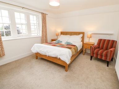 A bedroom with a wooden bed two nightstands with lamps a striped armchair and patterned curtains at Crookham Dairy in Crookham near Etal