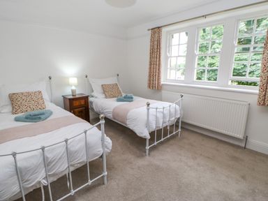 A bedroom with two single beds a wooden nightstand with a lamp and a window with curtains at Crookham Dairy Crookham near Etal