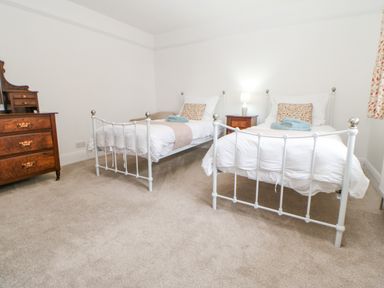 A bedroom with two white metal framed single beds a wooden nightstand with a lamp a wooden chest of drawers and carpeted floor at Crookham Dairy Crookham near Etal