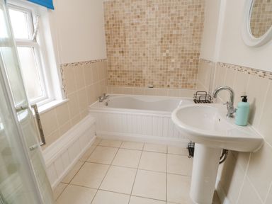 A bathroom with a bathtub a sink a window and tiled walls at Crookham Dairy in Crookham near Etal