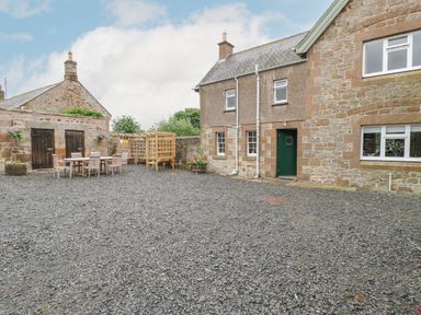 A gravel courtyard with stone buildings tables and chairs and a wooden pergola at Crookham Dairy in Crookham near Etal