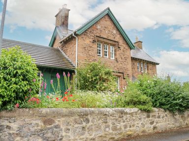 A stone house with green doors flowers and bushes in front at Crookham Dairy in Crookham near Etal