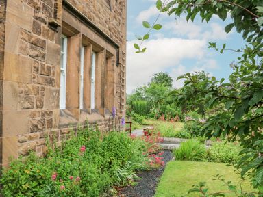 A garden with flowers and shrubs beside a stone building at Crookham Dairy Crookham near Etal