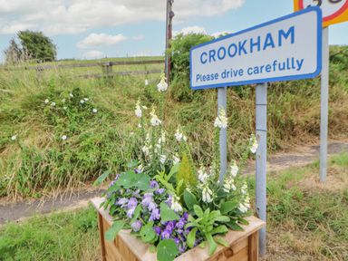 A roadside sign with flowers in a wooden planter and grass behind at Crookham near Etal