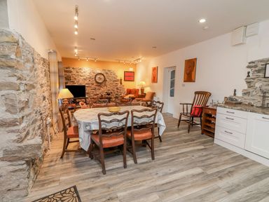 A dining area with a table and chairs next to a sitting area with armchairs and a television at The Artist's Barn in Ayle near Cappawhite