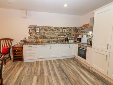 A kitchen with white cabinets stone wall and wooden floor at The Artist's Barn in Ayle near Cappawhite