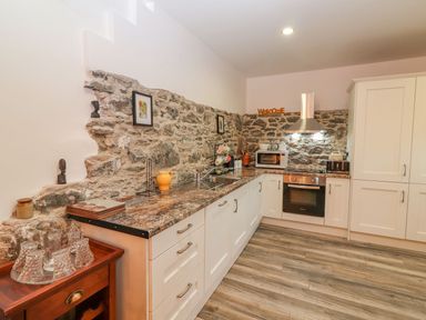A kitchen with stone walls white cabinets and wooden flooring at The Artists Barn in Ayle near Cappawhite