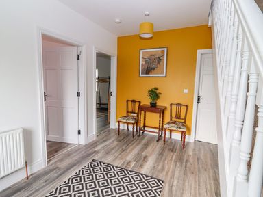 An entryway with a wooden table and two chairs against a yellow wall and a staircase to the side at The Artist's Barn in Ayle near Cappawhite