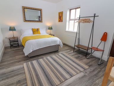 A bedroom with a bed with yellow pillow and throw two bedside tables with lamps a mirror a patterned rug a stand with hangers and a chair at The Artist's Barn in Ayle near Cappawhite