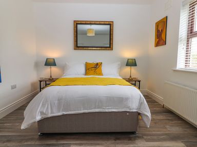 A bedroom with a double bed with white bedding and yellow accents lamps on bedside tables a mirror and a window at The Artist's Barn in Ayle near Cappawhite