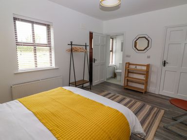 A bedroom with a bed with a yellow blanket a window a wooden shelf a clothing rack and a door leading to a bathroom at The Artist's Barn Ayle near Cappawhite