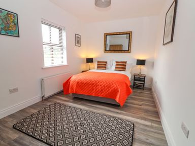 A bedroom with a bed with an orange cover and pillows two bedside tables with lamps a rug a window and wall art at The Artist's Barn in Ayle near Cappawhite