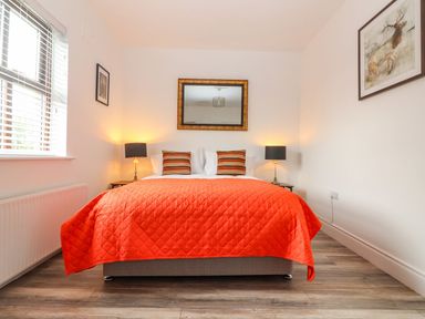 A bedroom with a bed covered by an orange quilt and striped pillows two lamps and paintings on walls at The Artist's Barn in Ayle near Cappawhite