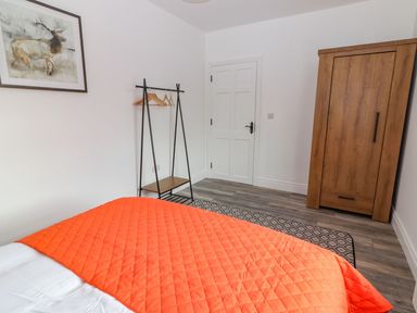 A bedroom with a bed covered by an orange quilt a wooden wardrobe a clothing rack with hangers a door and a framed animal painting on the wall at The Artist's Barn in Ayle near Cappawhite