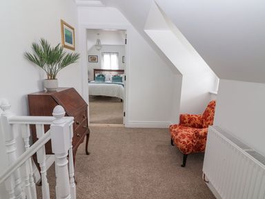 A hallway with a red patterned armchair and wooden desk with plant looking into a bedroom at The Artist's Barn in Ayle near Cappawhite
