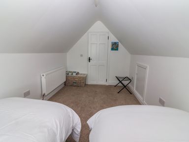 A bedroom with two beds a door a radiator a storage box and a luggage rack at The Artist's Barn in Ayle near Cappawhite