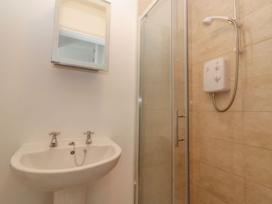 A bathroom with a white sink a mirror above and a glass shower enclosure with a shower unit at The Artist's Barn in Ayle near Cappawhite