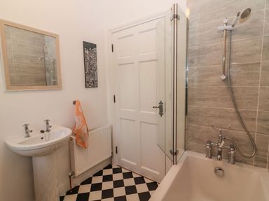 A bathroom with a sink a bathtub with shower and a door with black and white tiled floor at The Artist's Barn in Ayle near Cappawhite