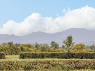 Fields with bushes and trees in front of mountains under a cloudy sky at The Artist's Barn in Ayle near Cappawhite