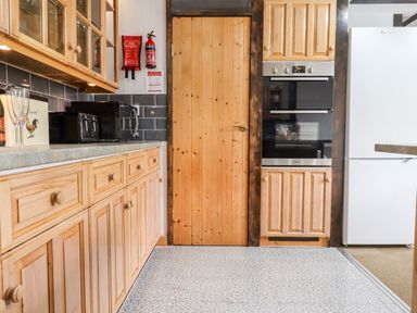 A kitchen with wooden cabinets a built in oven a wooden door and a white fridge at Foxglove Barn in South Brent