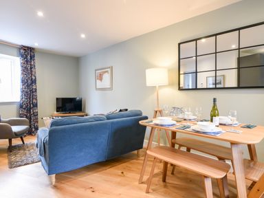 A living room with a blue couch a wooden dining table set with dishes and glasses and a floor lamp at Conybeare Cottage in Lyme Regis