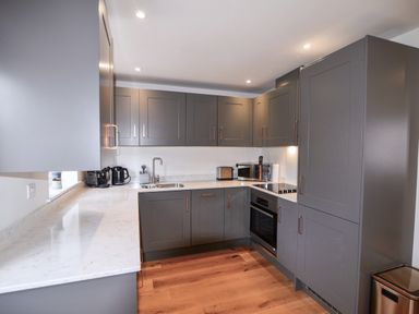 A kitchen with gray cabinets white countertops and wooden floor at Conybeare Cottage in Lyme Regis
