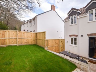 A fenced backyard with grass and a patio table with wine glasses outside a house at Conybeare Cottage in Lyme Regis