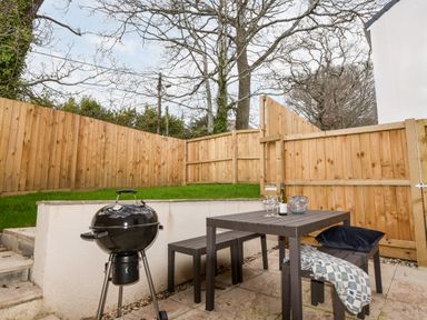An outdoor patio area with a charcoal grill a table and benches enclosed by a wooden fence