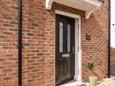 A black door with glass panels on a brick wall next to a potted plant at Conybeare Cottage Lyme Regis