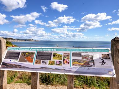 An informational sign about the Jurassic Coast World Heritage Site with the sea and cliffs in the background at Conybeare Cottage in Lyme Regis