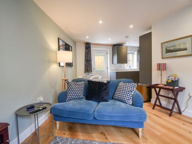 A living room with a blue sofa three cushions a floor lamp a small side table and a small wooden table with a lamp and books at Conybeare Cottage in Lyme Regis