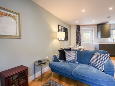 A living room with a blue sofa pillows a side table lamp and dining table in the background at Conybeare Cottage in Lyme Regis