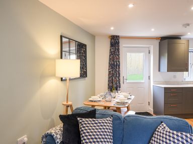 A dining table set with dishes and glasses next to a door with patterned curtains and a blue sofa with cushions at Conybeare Cottage in Lyme Regis