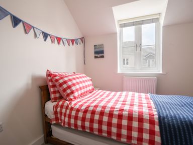 A bedroom with a single bed with red and white checkered bedding and a blue blanket under a window with a radiator at Conybeare Cottage in Lyme Regis