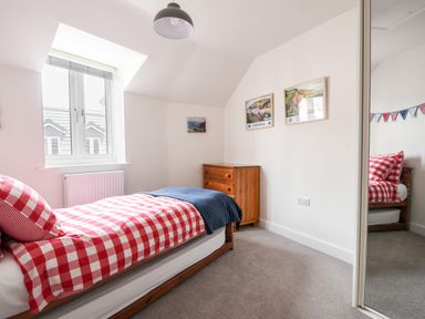 A bedroom with a single bed with red and white check bedding a wooden chest of drawers three framed pictures and a window at Conybeare Cottage in Lyme Regis