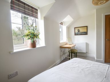 A bedroom with a bed a desk and chair a window with a vase of flowers and a painting on the wall at Conybeare Cottage in Lyme Regis