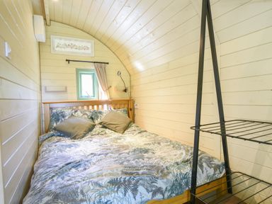 A bedroom with a double bed and two pillows next to a small window at Pendragon Pod in Axminster