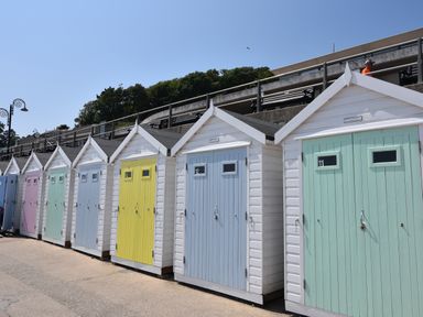 A row of colorful beach huts with numbered doors along a promenade at Pendragon Pod in Axminster