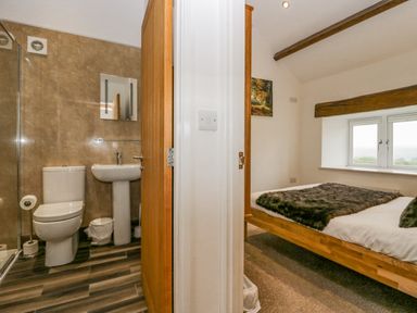 A bathroom with a toilet and sink next to a bedroom with a bed under a window at The Hidden Place in Watermillock near Pooley Bridge