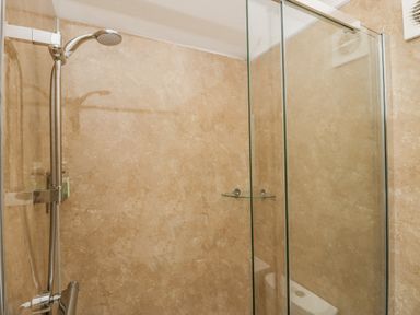 A shower area with a glass door a wall-mounted showerhead and beige tiled walls at The Hidden Place in Watermillock near Pooley Bridge
