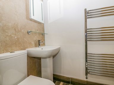 A bathroom with a toilet sink glass shelf mirror and towel radiator at The Hidden Place in Watermillock near Pooley Bridge