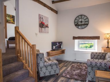 A living room with patterned armchairs a wall clock a small window and a television at The Hidden Place in Watermillock near Pooley Bridge