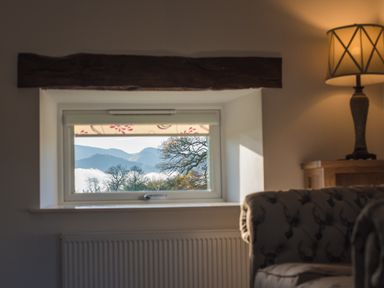 A window with a view of trees and mountains in a living room with a lamp and couch at The Hidden Place in Watermillock near Pooley Bridge