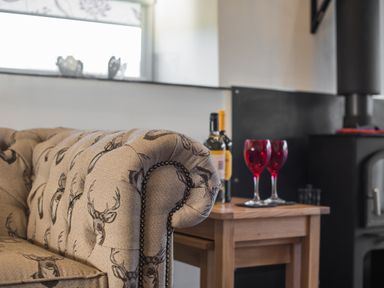 A close up of a patterned sofa arm next to a wooden side table with two red wine glasses and wine bottles at The Hidden Place in Watermillock near Pooley Bridge