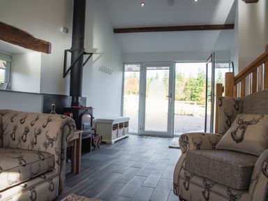 A living room with patterned armchairs a wood stove and glass doors opening to the outside at The Hidden Place in Watermillock near Pooley Bridge