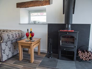 A corner of a room with a wood burning stove a small wooden table with wine bottles and glasses and a sofa at The Hidden Place in Watermillock near Pooley Bridge
